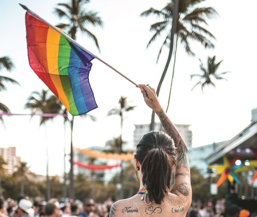 The back of a woman with tattoos waving a rainbow flag