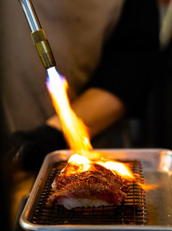 A Kokoro chef uses a blowtorch to scorch a set of three identical nigiri rolls (strips of rice topped with [usually raw] fish).