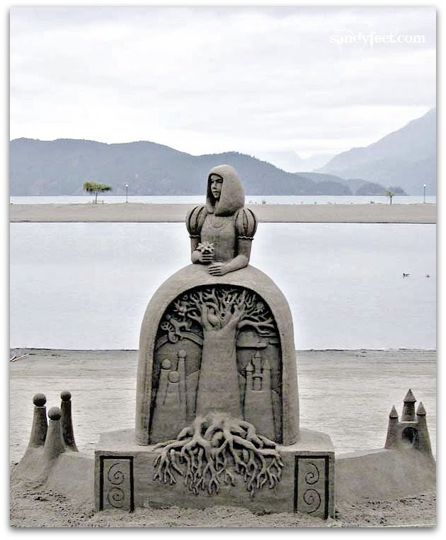 Sand sculpture showing an arch, the inside of which is filled with a tree and roots. On top of the arch is a woman.
