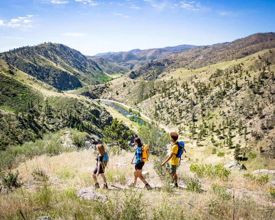 Three people hike on a ridge overlooking the Poudre Canyon.