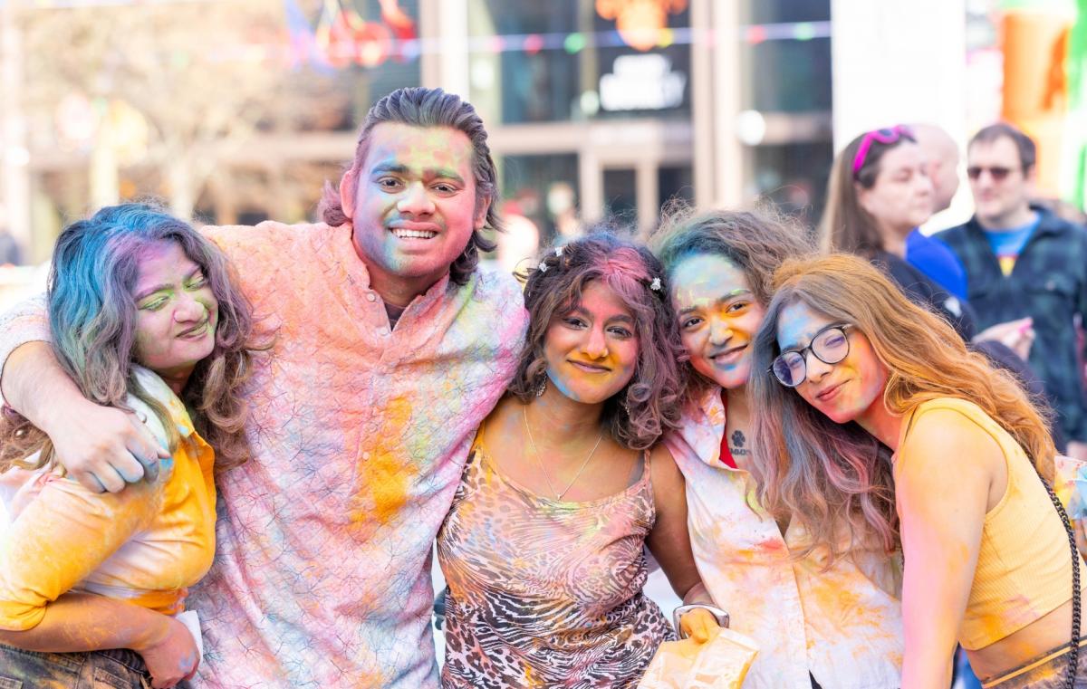 Group of friends covered in colourful powders posing for a photo at Holi event 2025
