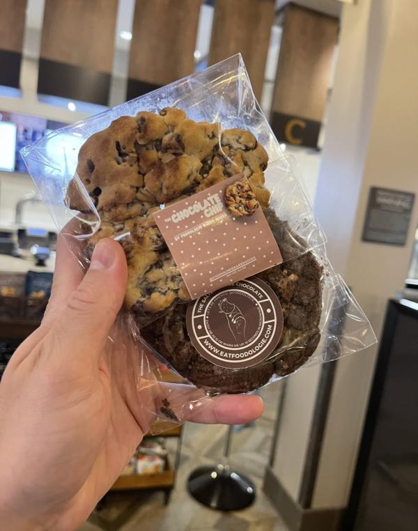 Two cookies being held up. The first cookie is at the top and chocolate chip. The second cookie is underneath the chocolate chip cookie and looks to be chocolate chocolate chip flavored.