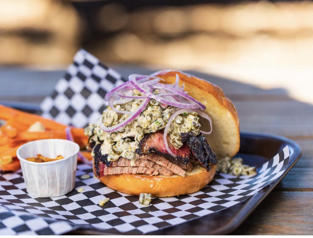 A sliced beef barbecue sandwich piled high with sauce and onions sitting on a plate.