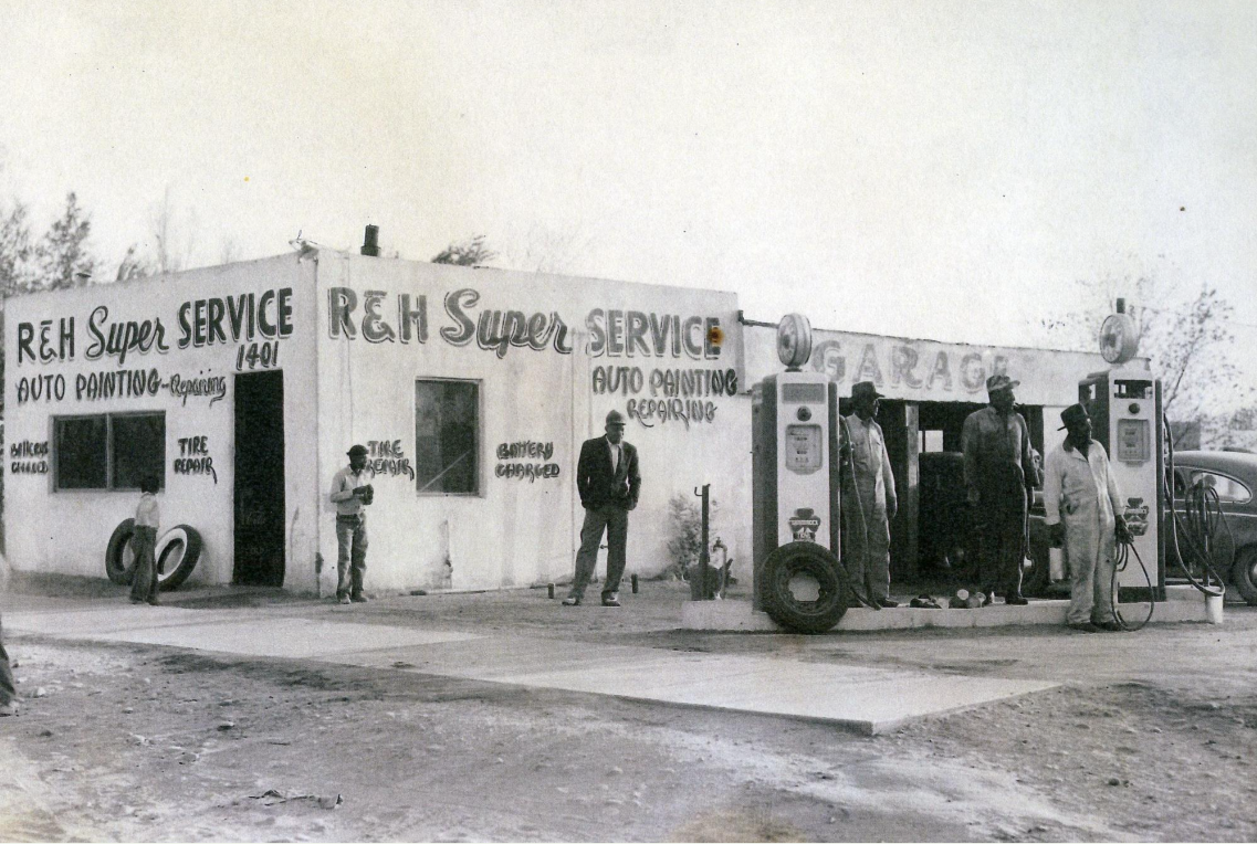Three men stand in front of a 1930s-built garage and service station in this black-and-white photograph. The sign reads "R and H Super Service, Auto Painting Repairing"