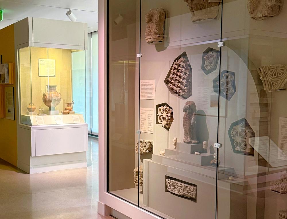 Display cases inside a museum with artifacts of figureings, a vase, and more unidentified objects sit inside.