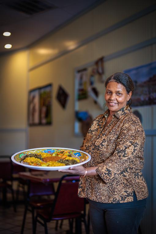 Haregu Bahtu standing in Mannaweenta's holding a plate of Ethiopian food