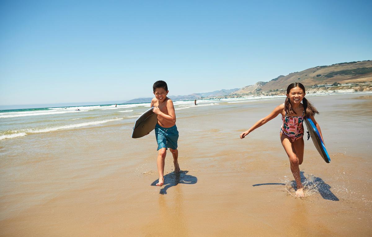 Two kids with boogie boards towards camera on the beach