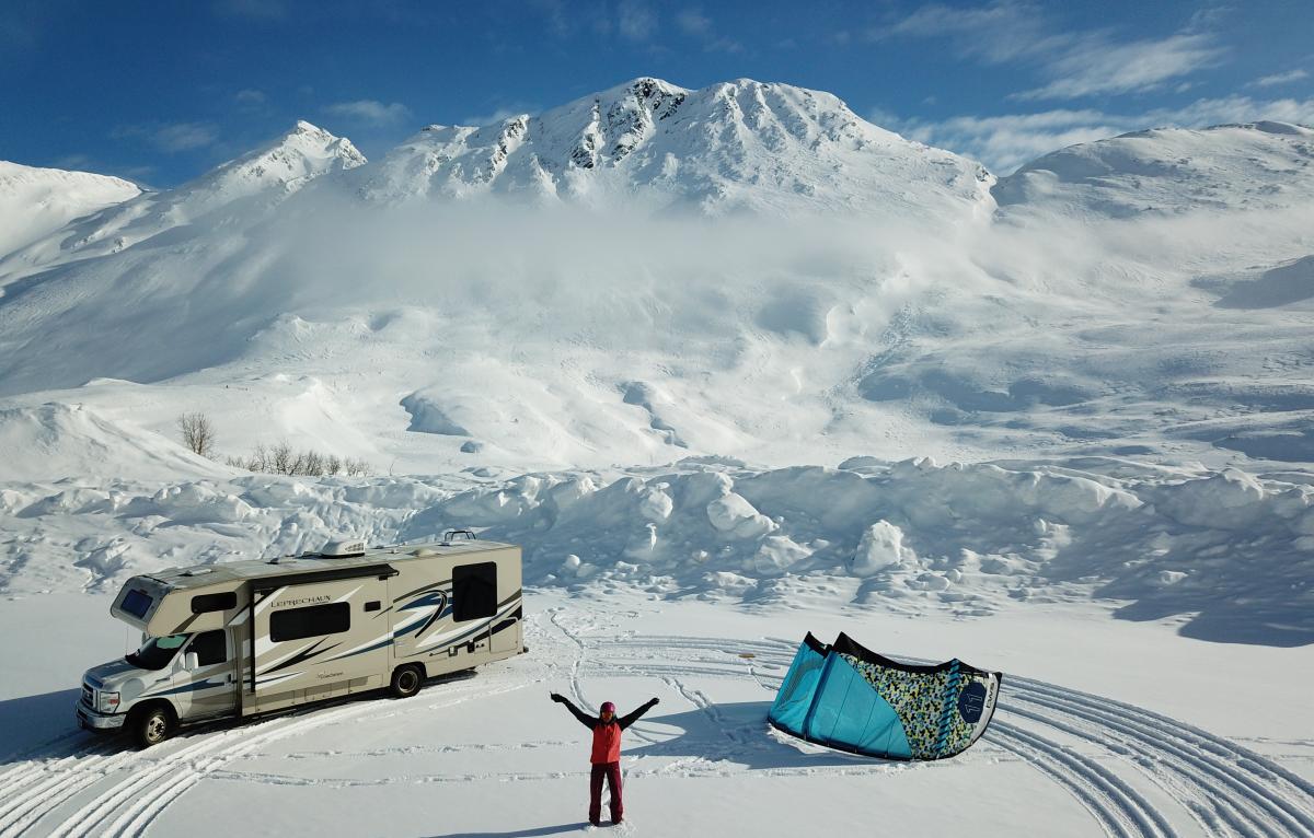 an RV parked next to a snowkite and person in a snowy mountain pass