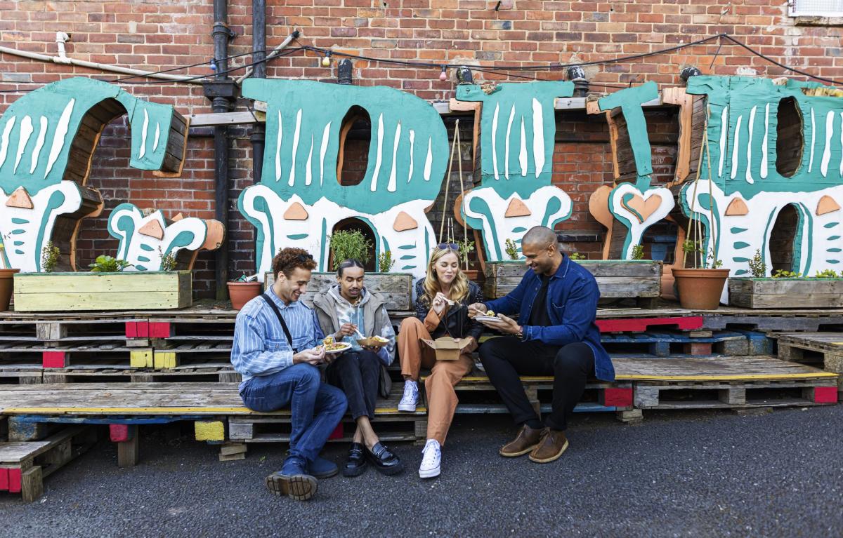 Group of friends sat eating in front of large sign reading 'GRUB'