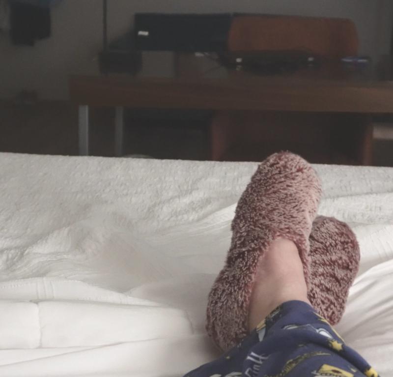 A person relaxing on a hotel bed in Cumberland County with their slippers on and feet crossed at the ankle.