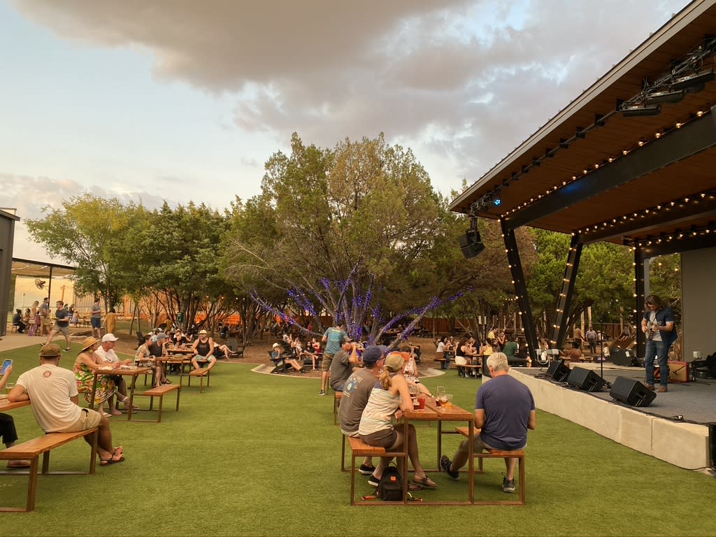 Image of people sitting at picnic tables at Meanwhile Brewing with an outdoor stage to the right.