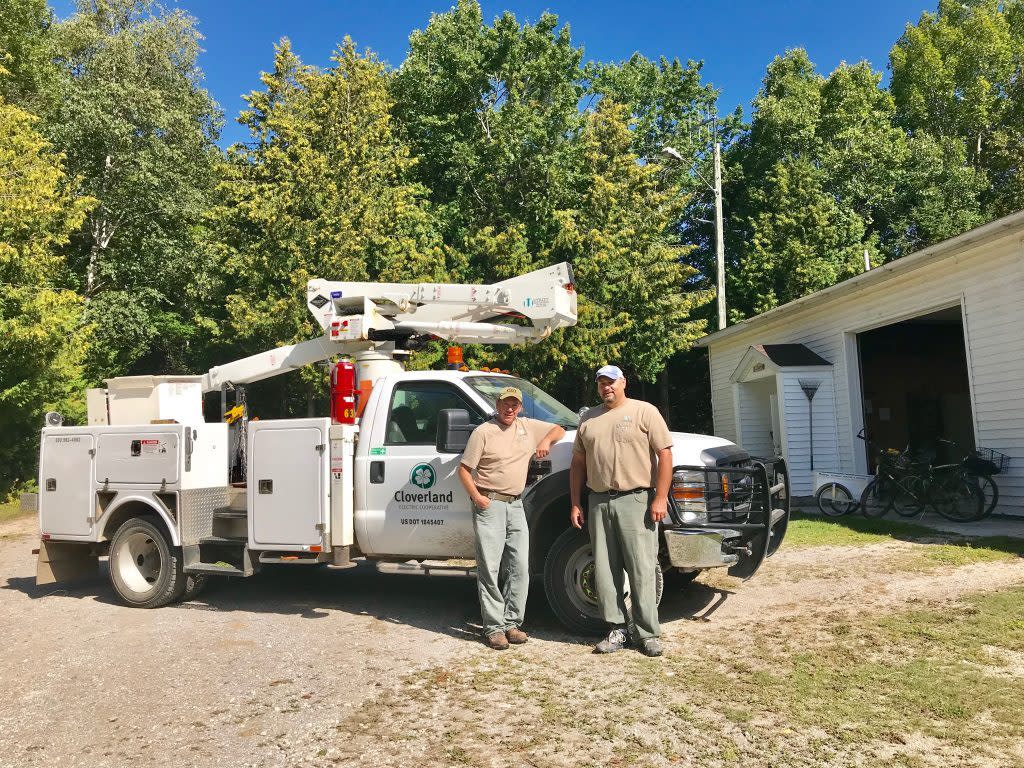 Two electrical line foremen stand by a Cloverland Electric Cooperative truck at the utility’s shop on Mackinac Island
