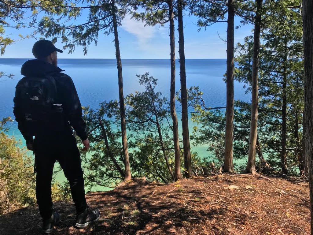A hiker pauses at the edge of a cliff overlooking the blue-green waters off Mackinac Island along Tranquil Bluff Trail
