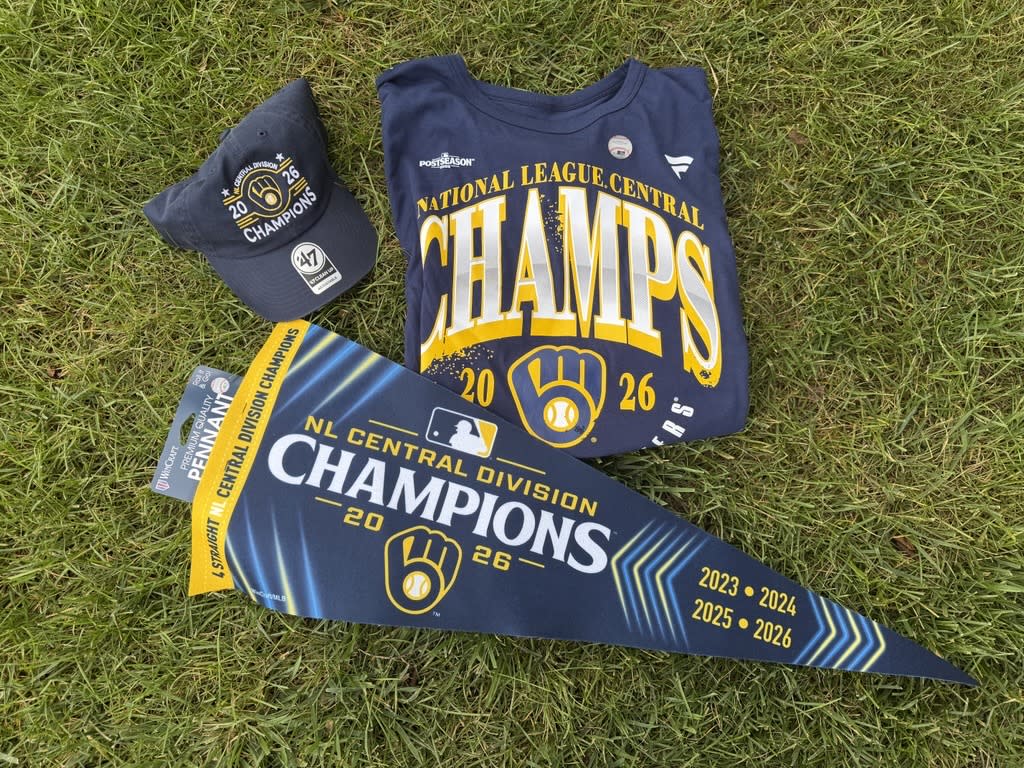 Milwaukee Brewers 2026 NL Central championship hat, T-shirt and pennant displayed on grass.