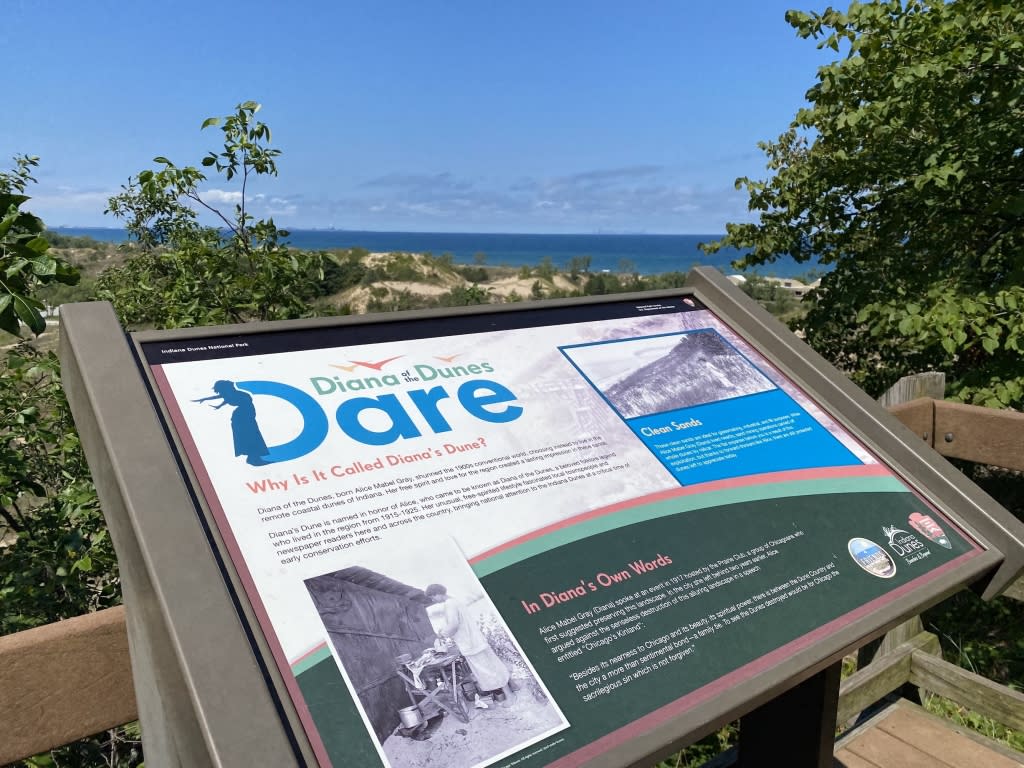 A scenic view of Lake Michigan is behind an informative sign about Diana of the Dunes
