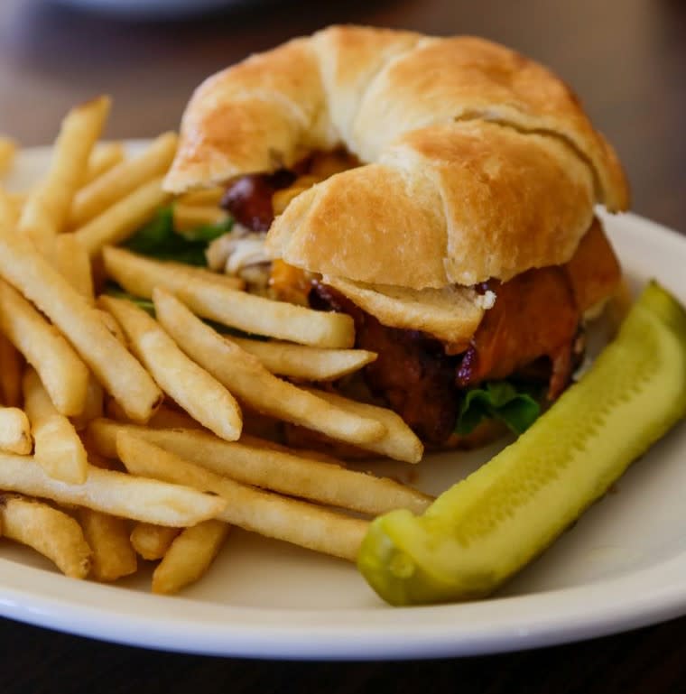 A croissant sandwich with fries and a pickle.