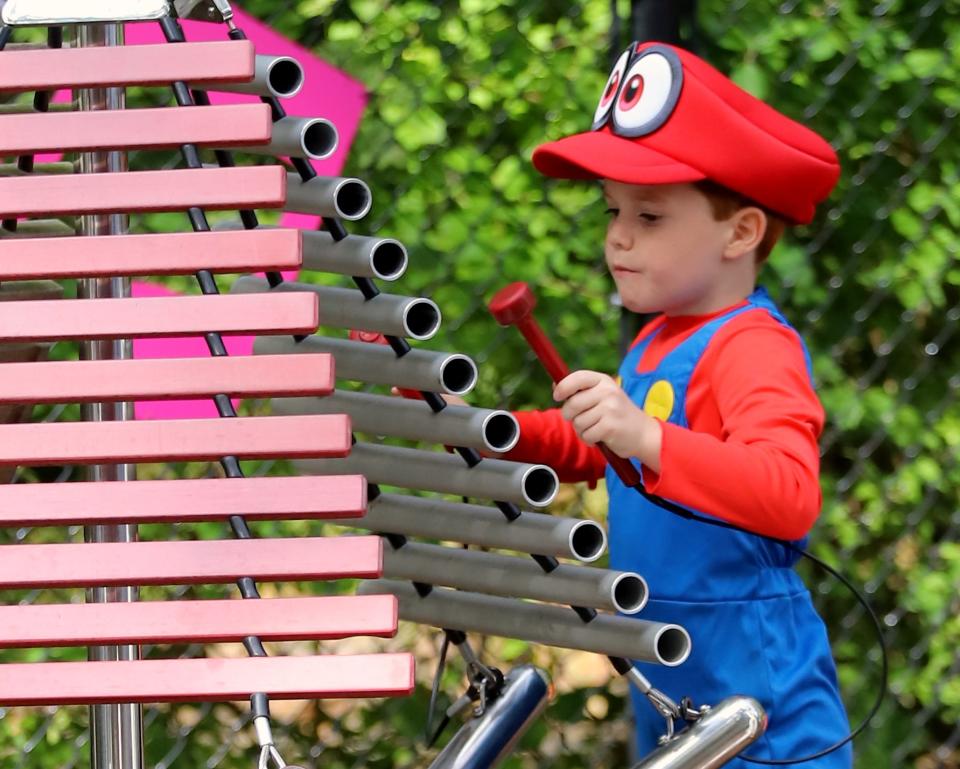 A toddler dressed in a Mario costume plays with instruments in the Percussion Garden at the Elmwood Park Zoo