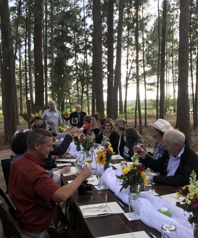 People Eating Together At A Long Table Surrounded By Trees in Fredericksburg, TX