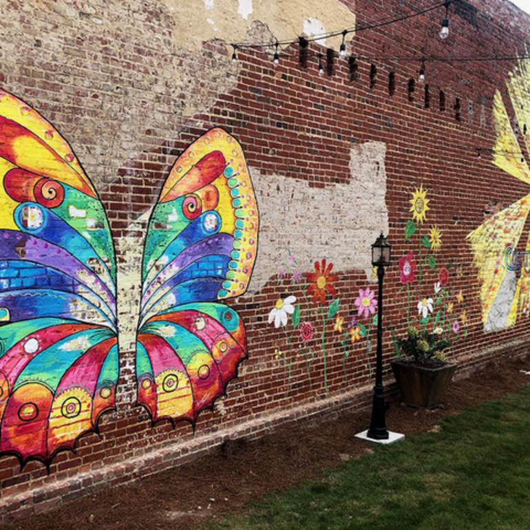 Vibrant mural of a butterfly and flowers on a brick wall with two street post in front of the wall in downtown Boaz.