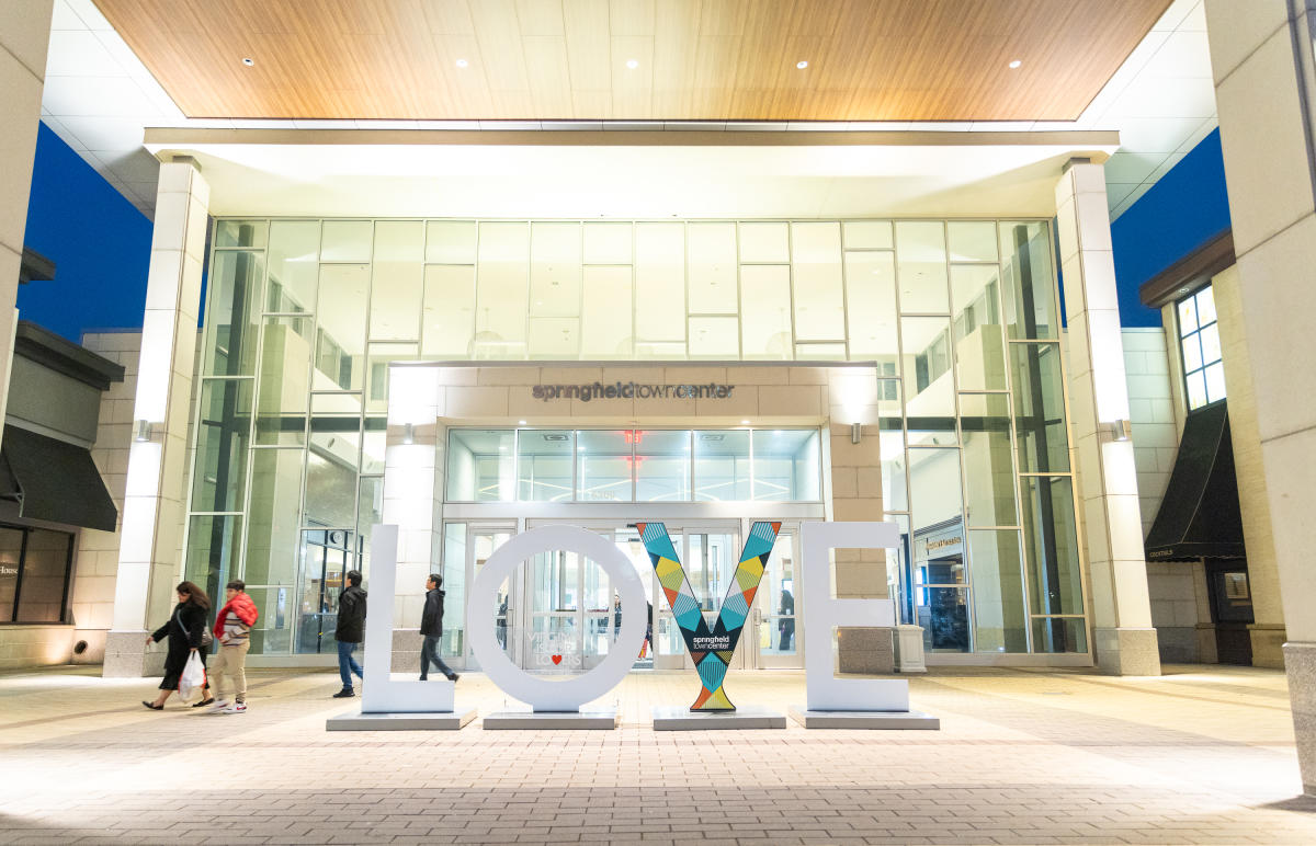 LOVEwork sign outside of the Springfield Town Center main entrance at night with people strolling around it