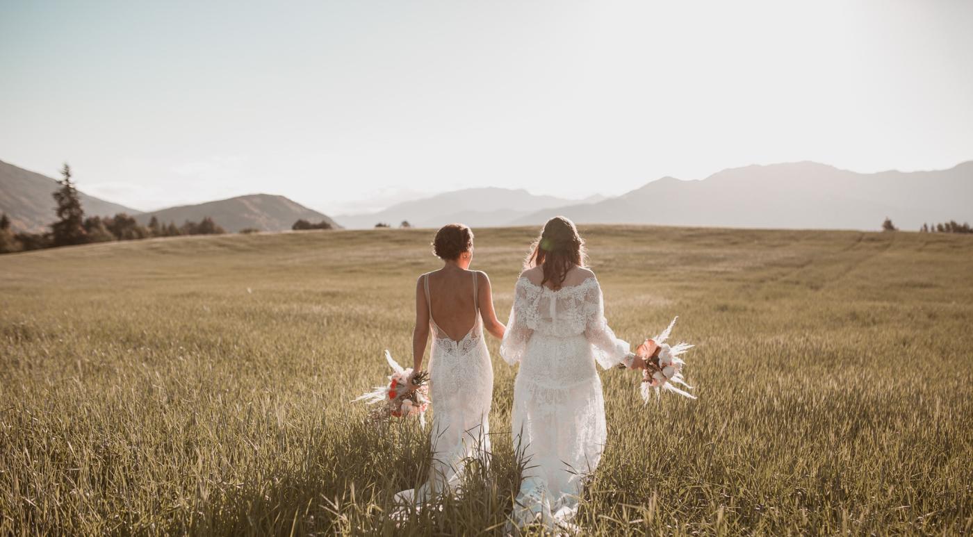 Married couple holding flower bouquet taking photographs in a grassy field near Queenstown