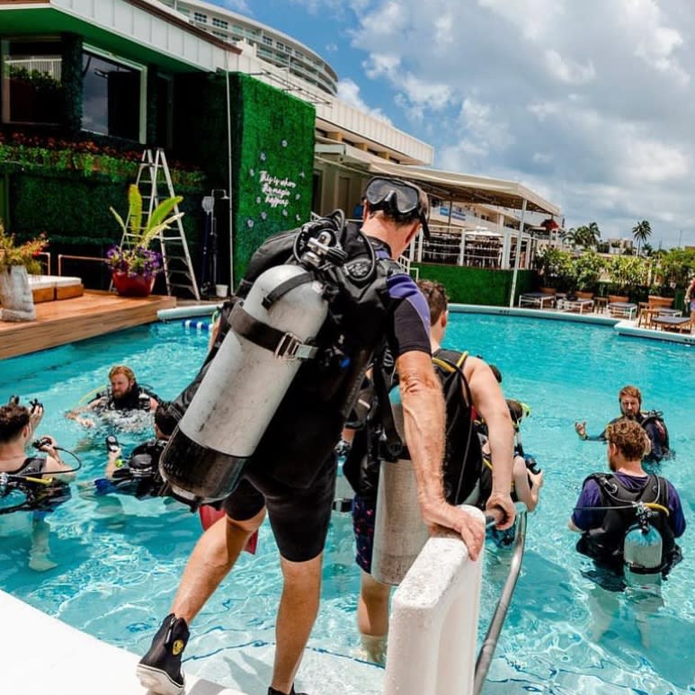 Adults in a pool wearing scuba gear for a dive lesson.