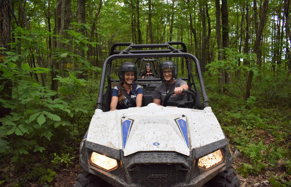 A group of women riding UTVs together in the woods.