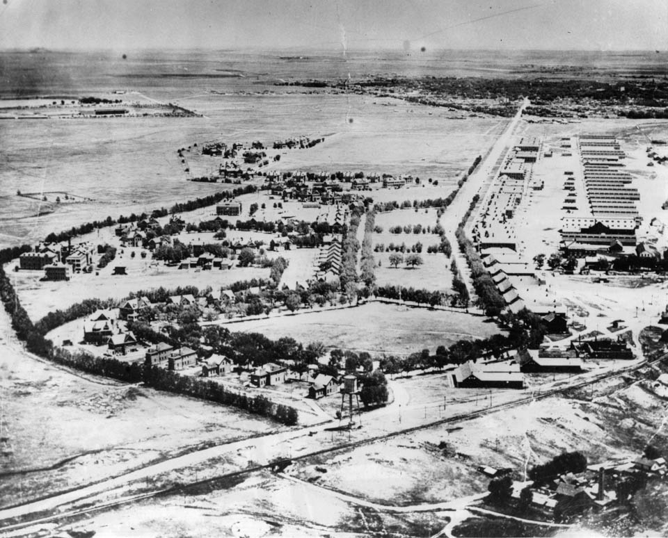 A black and white aerial view of a small town, For D.A. Russell, Wyoming, in the early 20th century. The town is surrounded by farmland and has a grid layout of streets, with a few buildings in the center of town.