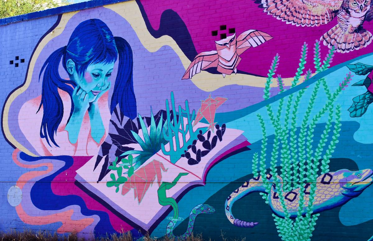 Close Up Photo of a colorful mural. A young girl is observing fantasy sea-life bursting from an open book in an aquatic themed mural.