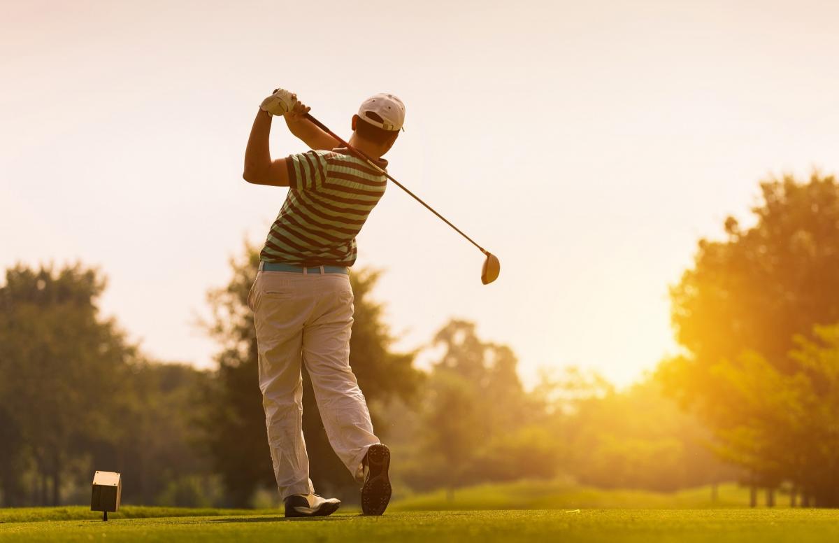 Golfer swinging a club with sunset in the background