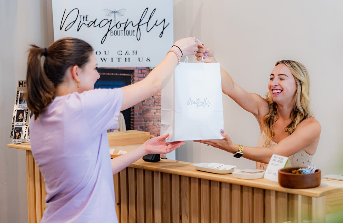 A young woman hands a shopping bag to another young girl at the Dragonfly Boutique in Smithfield.