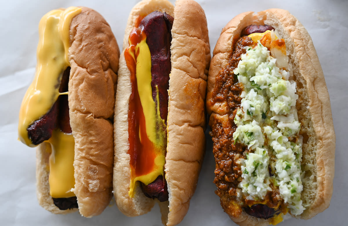 Three hot dogs with a variety of toppings including cheese, chili, slaw, and onions sit on a table at Jones Cafe.