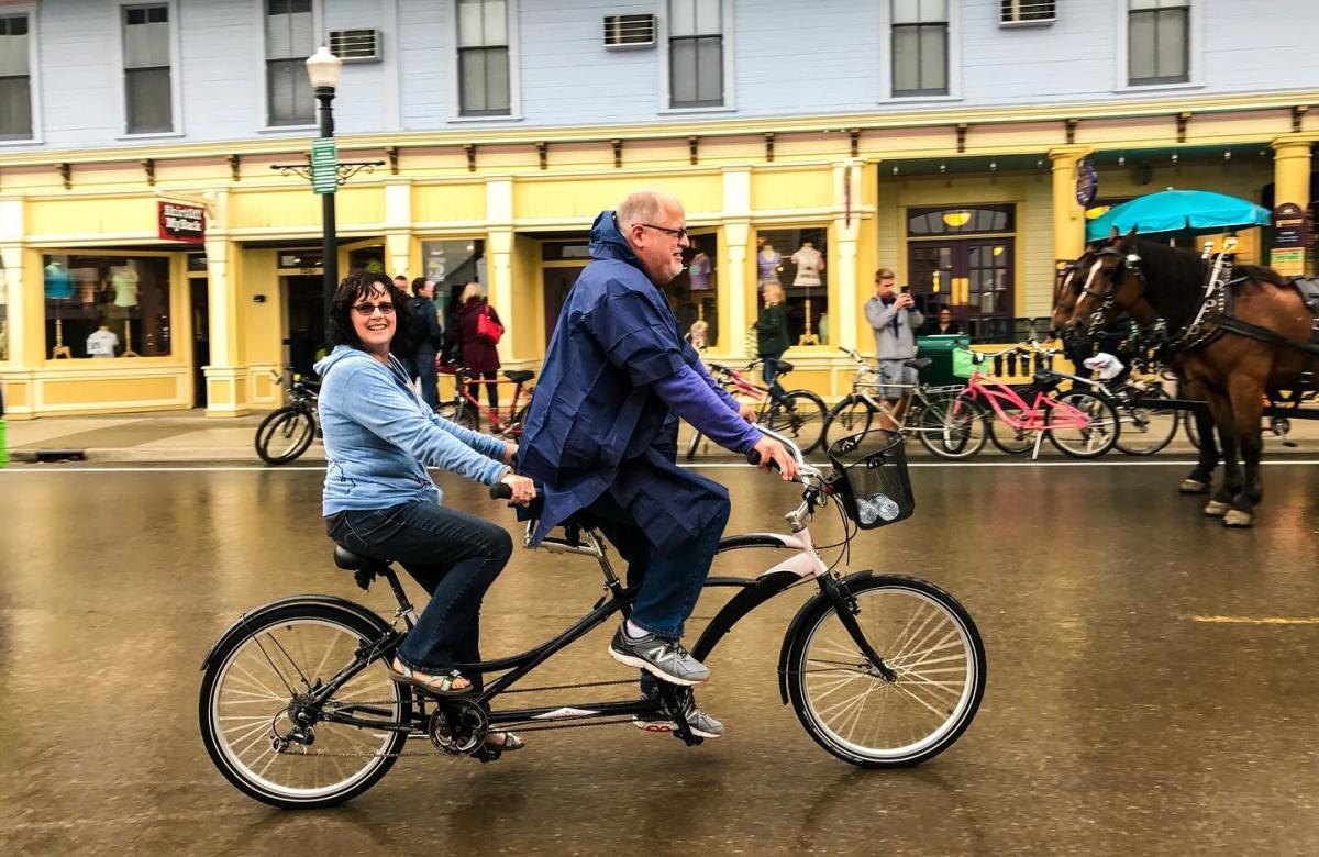 A couple pedals a tandem bicycle on a rainy Mackinac Island street