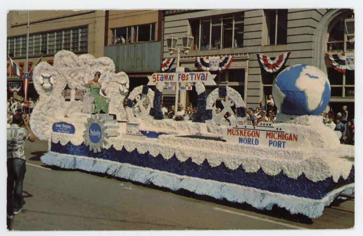 color photo of blue and white parade float carrying miss michigan , perhaps 1970s?
