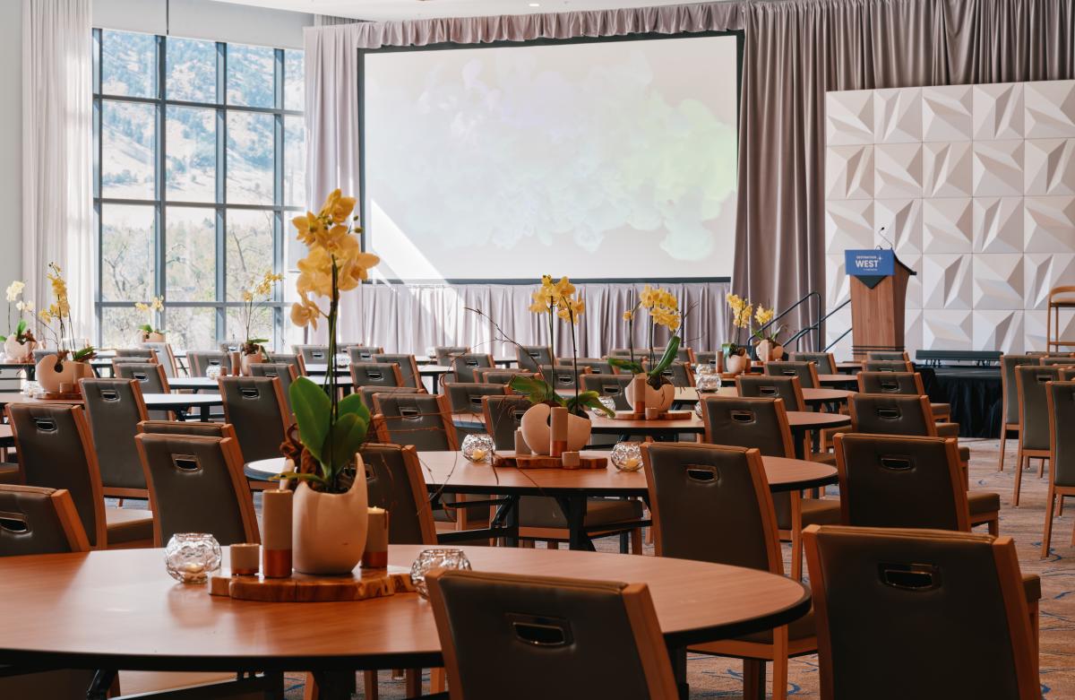 Limelight Boulder Flatirons Ballroom set in rounds for a conference, featuring floor-to-ceiling windows with mountain views, a presentation stage and screen, and elegant orchid centerpieces