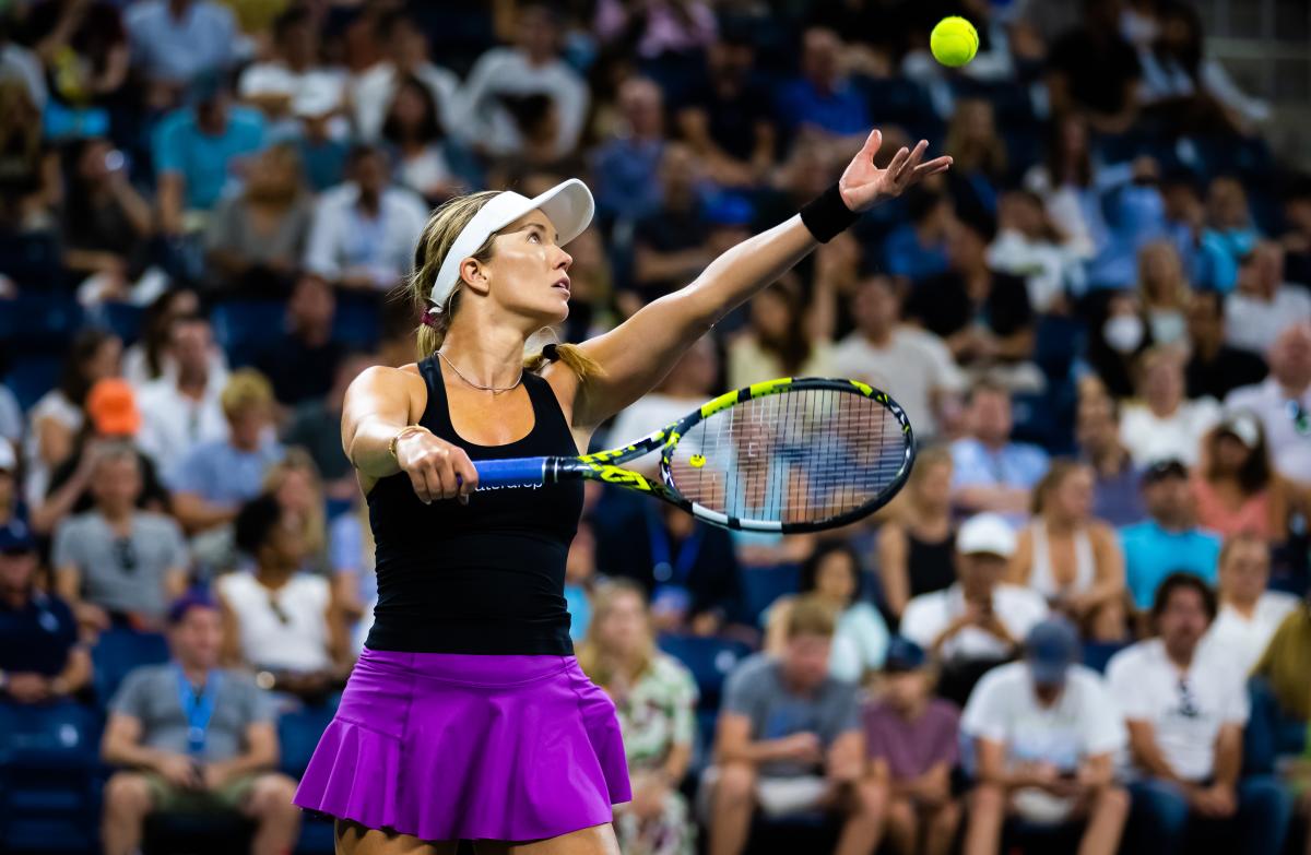 Woman tossing tennis serve in the air with focused crowed in the background.