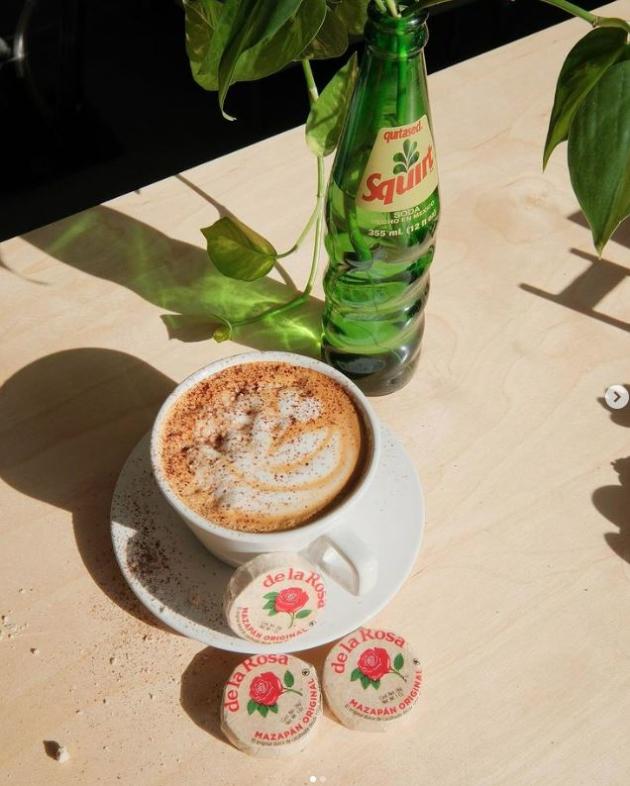 Cup of coffee with marzepan treats and bottled sparkling water next to it