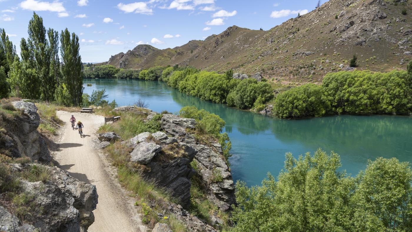 People biking Roxburgh Gorge Trail next to vibrant blue river