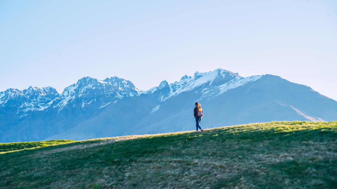 Female in the distance on a walking trail with snow capped mountain in the background