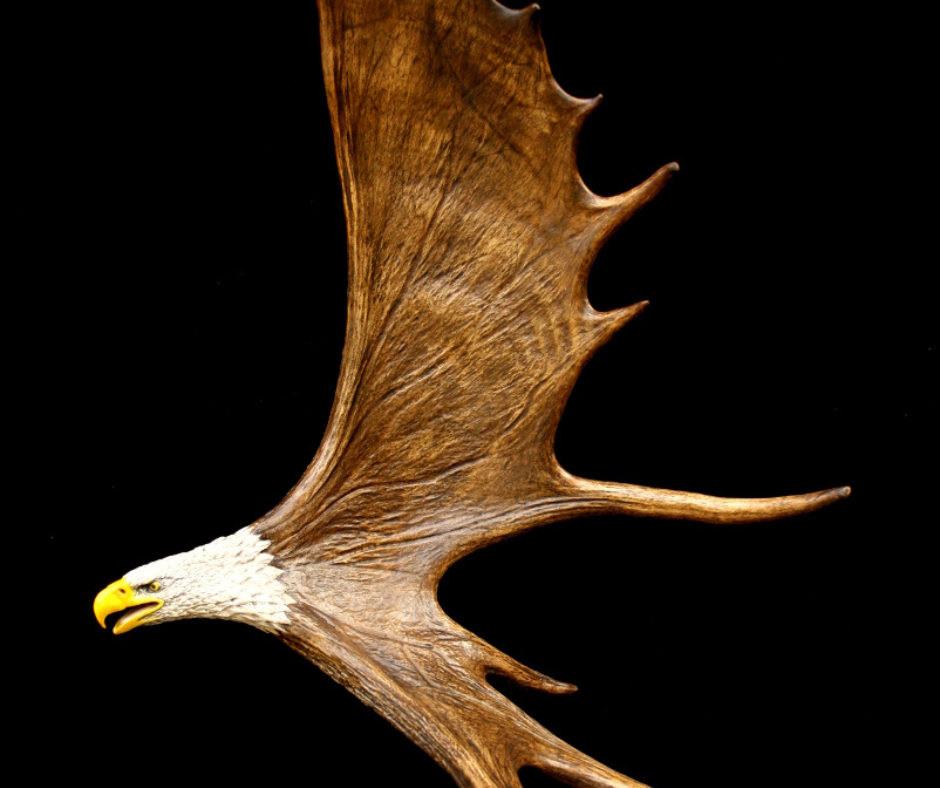 A detailed antler carving depicting an eagle in flight, showcasing intricate textures and artistry against a dark background.