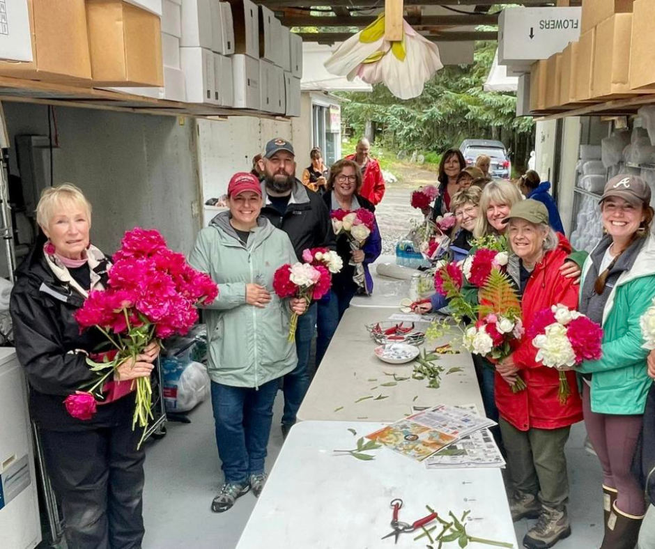 A group of cheerful individuals inside a workshop, each holding bright pink and white peony bouquets, enjoying a flower arranging session.