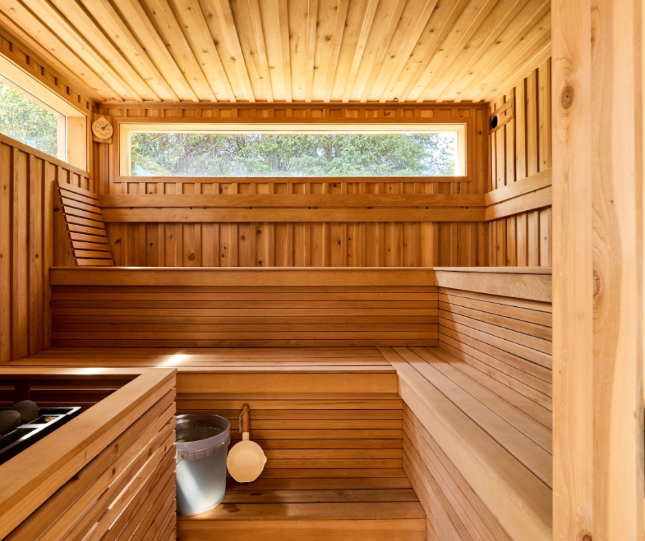 A cozy wooden sauna with natural light streaming in from a window, featuring a bucket of water and traditional wooden benches, creating a warm and inviting atmosphere.