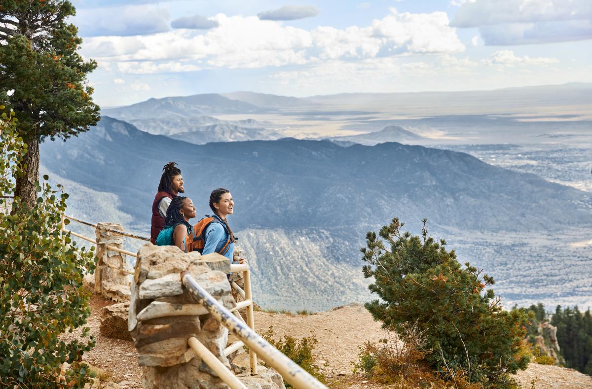 Three people look out over Albuquerque from atop the crest on the Sandia Mountains.