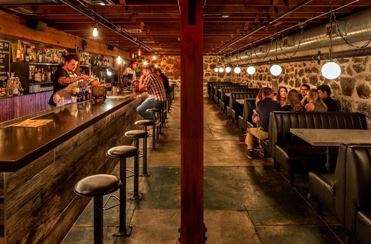 Dim, narrow basement bar with booths and a bar with stools