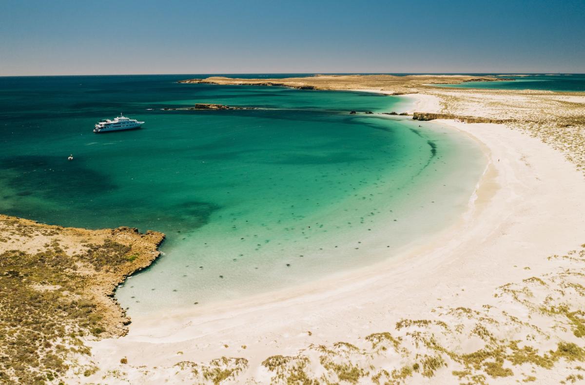 Taken from a vantage point higher than the beach, the image shows the beach, clear waters and True North at anchor on one of the Montebello Islands