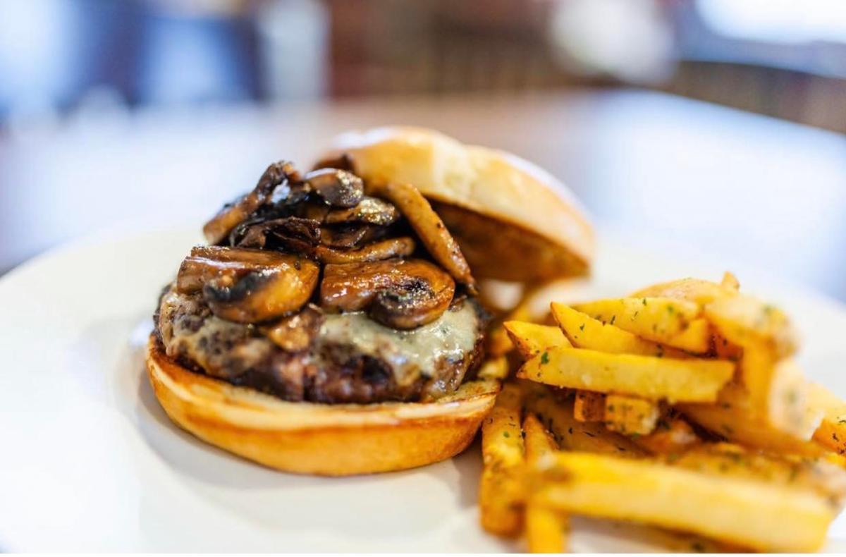 A cheeseburger is topped with sauteed mushrooms with a side of fries at The Kitchen
