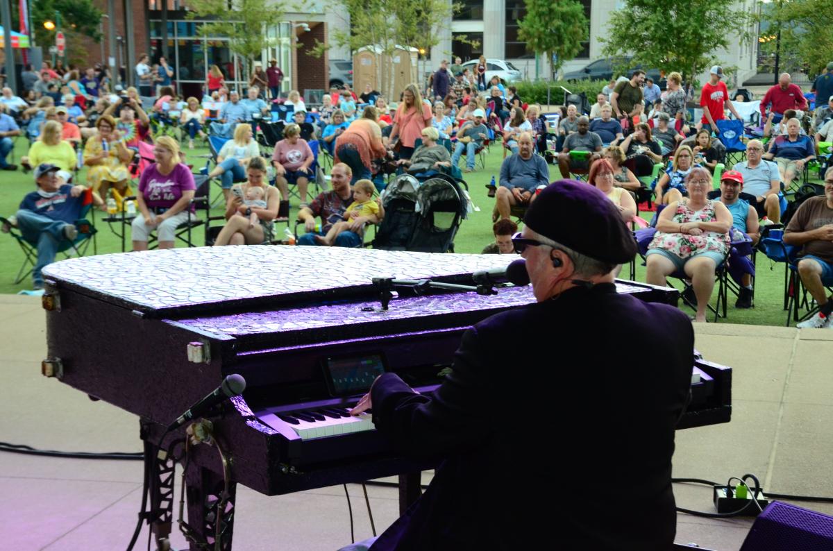 people sitting at an outdoor concert with a piano