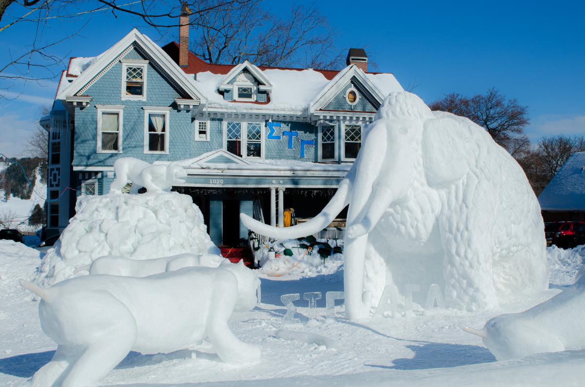 a saber tooth tiger and mastodon made of snow face off in front of a fraternity house