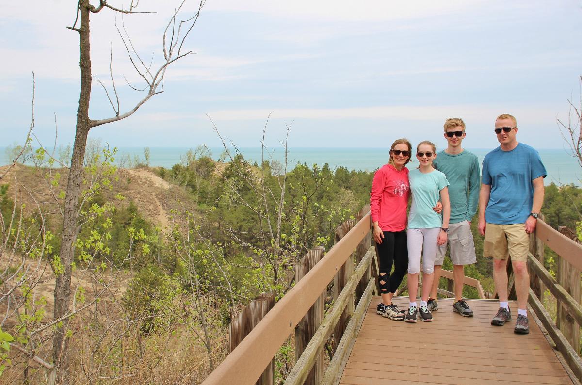 A family of four stands in front of a landscape of plant-covered dunes and Lake Michigan.