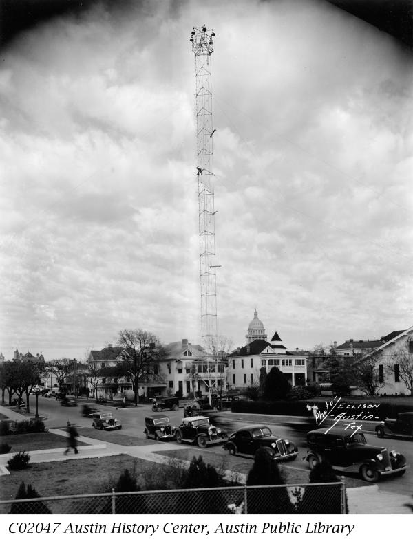 Historic black and white photo of a Moonlight Tower in Austin with 1930s era cars in foreground